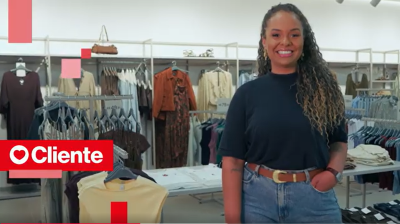 Mulher com camiseta preta e calça jeans em frente a arara de roupas na loja